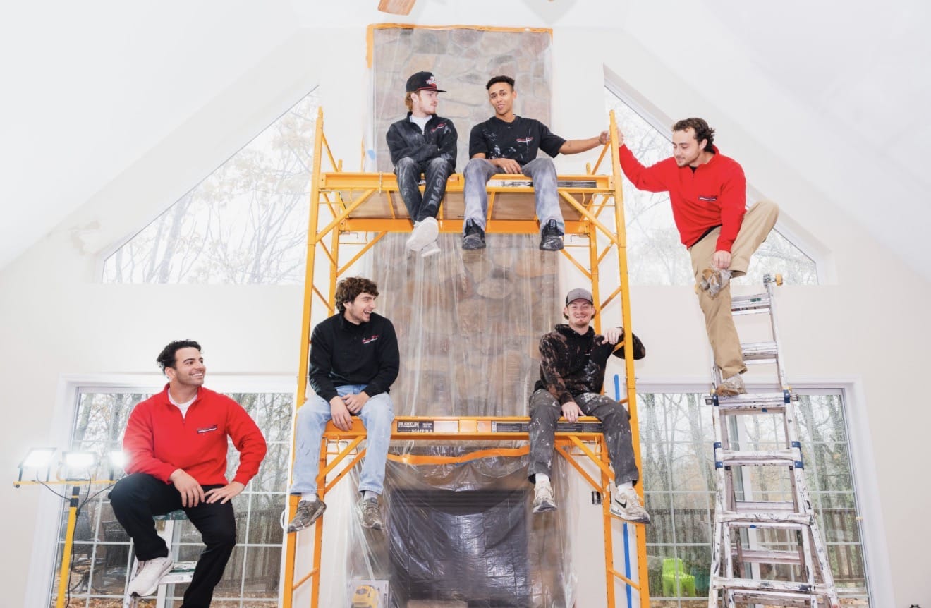 Professional Painting Team for High Ceiling Interior Painting A professional painting team poses on scaffolding in a large, high ceiling room, ready for interior painting.