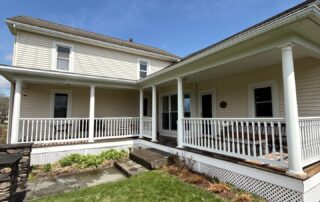 A large two story house with light yellow siding and a wide wrap around porch with white railings. how long does exterior paint last